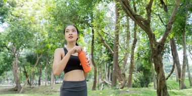 Zengin bir parkta ferahlatıcı bir mola veren Asyalı kadın egzersiz yaptıktan sonra susuz kalmaya hazırlanıyor..