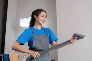 Gülümseyen bir temizlikçi modern bir evde temizlik işleri için elektrikli süpürge hazırlıyor..