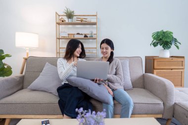 Lezbiyen bir çift, oturma odalarında dizüstü bilgisayar kullanırken eğleniyor, neşe ve bağlantı anlarını paylaşıyor..