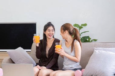 İki kadın, rahat bir ev ortamında yan yana oturup kahkahalar atan canlı bir sohbet ve portakal suyu seviyor..