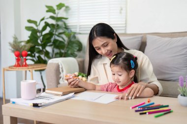 Asyalı anne, genç kızına bir çizim aktivitesinde rehberlik eder, yaratıcılığı teşvik eder ve sıcak bir yuva ortamında bağ kurar..