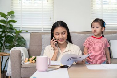 Asyalı anne, kızıyla bir telefon görüşmesi yaparken birden fazla iş yapar. İş ve aile ortamını rahat bir şekilde harmanlar..
