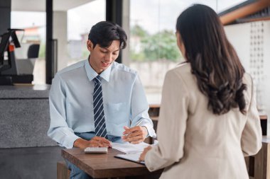 Bir erkek ve kadın, bir kafede iş görüşmesi yapıyor. Stratejik planlama ve belgelendirme üzerine odaklanıyorlar. Günlük, işbirlikçi bir atmosfer içinde..
