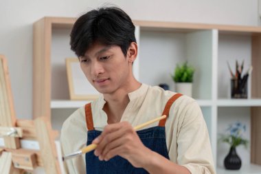 Odaklanmış genç ressam, sanatsal konsantrasyon ve tekniği ilham verici bir çalışma alanında gösteren bir tuval üzerinde dikkatle çalışıyor..