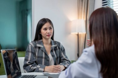 Odaklanmış genç bir kadın, parlak bir sağlık hizmetleri bürosuna güven sağlamak ve anlayış iletmek için bir doktoru dinler..