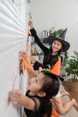 Cadı şapkalı bir anne ve kız Cadılar Bayramı için evlerini dekore ediyor, neşeli atmosferin ve yaratıcı bağlılık zamanının tadını çıkarıyorlar..