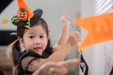 Cadı şapkalı genç bir kız cadılar bayramı için evini dekore etmesine yardım ediyor. Etrafı renkli afişlerle çevrili ve festival atmosferinin tadını çıkarıyor..