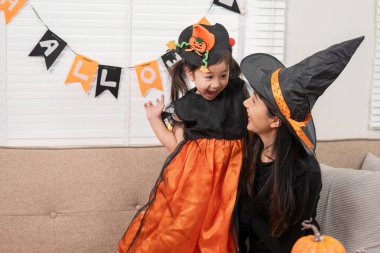 Cadı şapkalı bir anne ve kız evde neşeli bir cadılar bayramı kutlaması paylaşıyor, etrafı şenlikli süslemeler ve balkabaklarıyla çevrili..