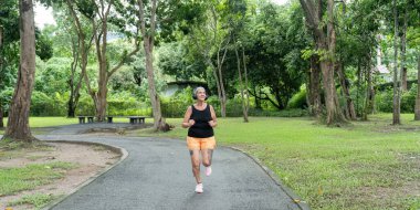 Yeşil ve ağaçlarla çevrili sakin bir parkta sabah koşusundan zevk alan yaşlı bir kadın sağlıklı ve aktif bir yaşam tarzını teşvik ediyor..