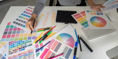 Bir grafik tasarımcısı titizlikle bir masanın üzerinde çeşitli renk örnekleri ve tasarım araçları düzenliyor, yaratıcılığı ve detaylara dikkat çekiyor.