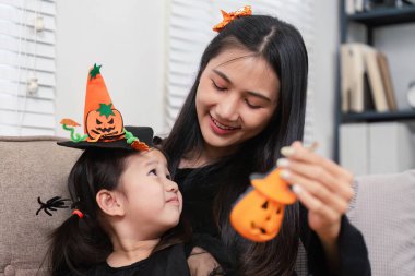 Asyalı bir anne ve kız Cadılar Bayramı el sanatları ve süslemelerinin keyfini çıkararak, şenlikli ev ortamlarında sevgi dolu bir anı paylaşıyorlar..