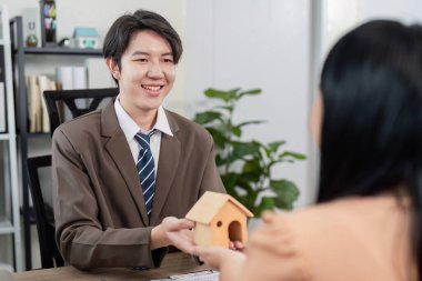 Bir emlakçı müşterisiyle emlak satışı tartışmasını kolaylaştırarak, müşterilerin ev sahipliği hedeflerine ulaşmaya odaklanır..