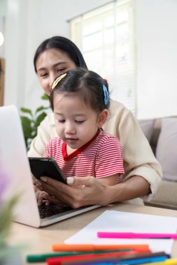 Bir anne, çocuklarının bilgisayar ve akıllı telefon gibi dijital araçlarla iletişim kurmasını teşvik eder..