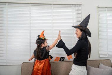 Bir anne ve kız Cadılar Bayramı 'nı, uyumlu cadı kostümleri giyip neşeli bir beşlik çakarak kutluyorlar..