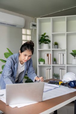 Dinamik bir kadın mühendis, verimliliği ve uygulama stratejilerini geliştirmek için dijital içgörüler ve bir dizüstü bilgisayar kullanarak proje planlamasına girişiyor..