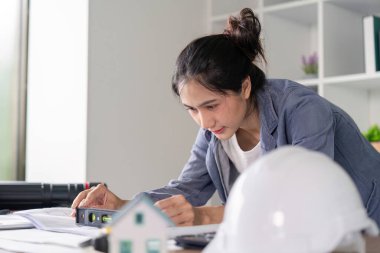 Odaklanmış bir kadın mühendis, ofis işlerinde hassasiyet ve dikkati vurgulayarak mimari planları analiz etmek için bir seviye aracı kullanır..