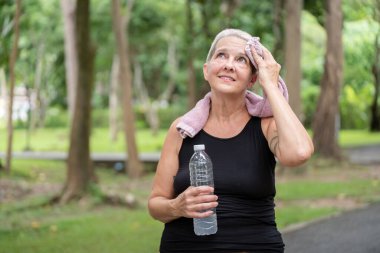 Son sınıf öğrencisi bir kadın, ferahlatıcı bir koşuya katılırken, susuzluk ve doğa barışını vurgularken, kendi kendine bakım ve sağlıklı yaşlanma deneyimi yaşar..