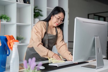 A housekeeper skillfully cleans an office desk and accessories, ensuring an orderly and dust free environment for productivity. clipart