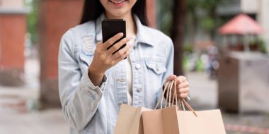 Teknoloji düşkünü bir müşteri elinde alışveriş poşetleri tutarken akıllı telefonunu kontrol ediyor. Kara Cuma hazırlıklarını ve dijital bağlantılarını gösteriyor..
