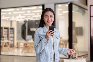 Gülümseyen bir müşteri akıllı telefonunu kullanır, Kara Cuma 'yı kutlarken birden fazla alışveriş torbası bulur, modern perakende neşesini somutlaştırır..