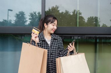 Bir tüketici Kara Cuma alışverişinin heyecanını yaşıyor, bir kredi kartı kullanıyor ve elinde sayısız torba tutuyor, mevsimsel perakende heyecanını sembolize ediyor.