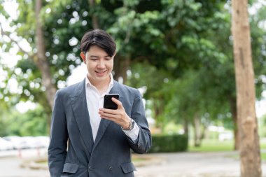 İş iletişimi için açık havada akıllı telefon kullanan genç bir profesyonel, bağlantıyı ve modern iş uygulamalarını vurguluyor.