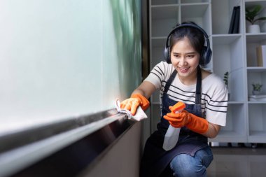 Müzik dinlerken tozluk kullanan neşeli bir temizlikçi ev temizliği ve bakımına canlı bir yaklaşımı sembolize eder..