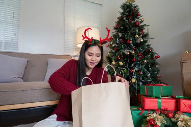 Ren geyiği boynuzu takan neşeli bekar bir kadın Noel ağacının yanında bayram hediyelerini açıyor, kendini kutlamaya ve mutluluğa odaklanıyor..