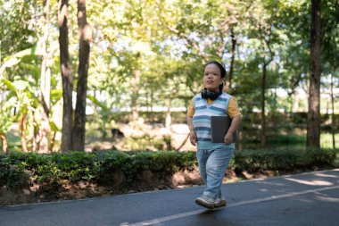 Achondroplasia 'lı Asyalı bir kadın orman parkında kulaklıklarla yürümekten keyif alıyor, bireysellik ve sükuneti canlandırıyor..