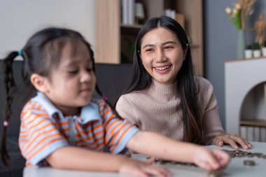 Asyalı anne gururla kızının para biriktirmesini izliyor, mali eğitimi teşvik ediyor ve evde pembe bir kumbara ile bağ kuruyor.