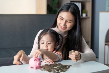 Asyalı anne ve kızı mutlu bir şekilde evdeki pembe domuz kumbarasında para biriktirip birlikte keyifli bir eğitim anı yaşıyorlar..