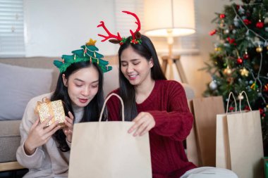 Lezbiyen Asyalı çift, Noel ağacının yanındaki bir şenlik ortamında hediyelerini açıyor, neşe ve bayram neşesini paylaşıyorlar..
