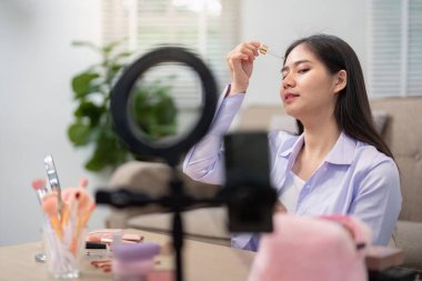 Kameranın önünde cilt bakımı uygulayan Asyalı bir kadın kapalı alanda güzellik tavsiyeleri veriyor..
