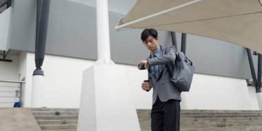 Asyalı bir adam elinde kahve tutup telefonunu kontrol ederken şehir iş ortamında birden fazla iş becerisi sergiliyor..