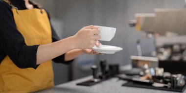 Kafede kahve fincanı ve çay tabağı tutan bir baristanın yakınına. Müşterilere özenle hizmet etmeye hazır..
