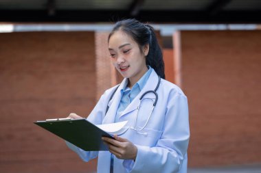 Asyalı kadın doktor boynunda steteskopla profesyonel bir ortamda dokümanları inceliyor..