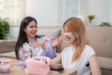 İki Asyalı kadın gülüyor ve makyaj seansından zevk alıyorlar. Arkadaşlık ve eğlenceyi vurguluyorlar..