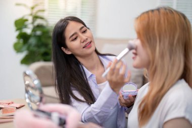 Neşeli bir Asyalı kadın arkadaşına allık sürüyor. Eğlenceli bir makyaj seansının bir parçası..