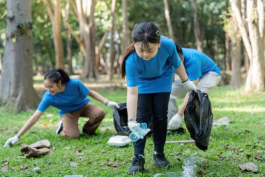 Aile ve gönüllüler aktif olarak parkta çöp topluyorlar, takım çalışması ve çevre bakımını vurguluyorlar..