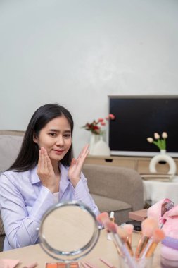 Asyalı güzellik blogcusu cildini makyaj uygulaması için hazırlıyor, evde bir video dersinde cilt basamaklarını gösteriyor.