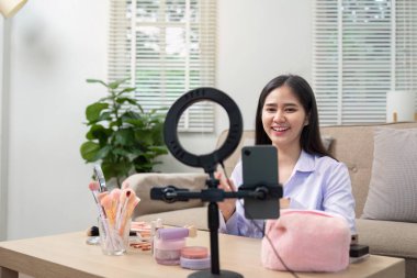 Asyalı güzellik uzmanı makyaj vlog 'u sırasında kameraya gülümsüyor. Ev ortamında dostane ve misafirperver bir ortam yaratıyor..