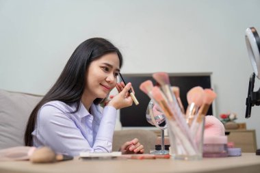 Asyalı güzellik uzmanı, kozmetik tekniklerinde uzmanlığı vurgulayan bir video yayınını çekerken makyajı ustalıkla uygular..