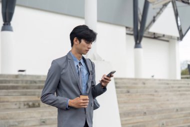 Asyalı işadamı dışarıda elinde kahve ile akıllı telefonunu kullanarak profesyonel ve gelişigüzel elementlerin bir karışımını çiziyor..