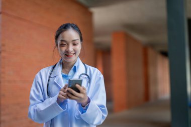 Bir doktor, sağlık hizmetlerinde teknolojinin entegrasyonunu gösteren bir klinikte akıllı telefonunu kullanırken gülümsüyor..