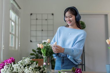 Bir kadın neşeyle çiçekleri rahat bir evde düzenliyor yaratıcılığını ve doğaya olan sevgisini sergiliyor..