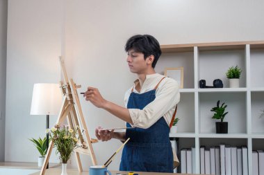 Odaklanmış genç bir sanatçı, yaratıcılığını kapalı bir stüdyoda tuvale yansıtıyor..