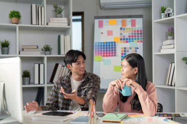 Bir tasarım ekibi, canlı bir ofiste fikir ve yaratıcılık alışverişinde bulunan grafik projeleri üzerinde işbirliği yapar..