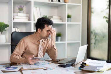 Bir adam yoğun bir ofiste stresle ve aşırı çalışmayla mücadele ediyor. Modern iş hayatının zorluklarını vurguluyor..