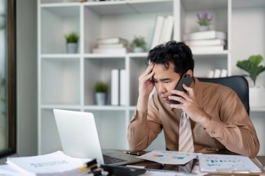 Stresli bir işadamı yoğun bir ofis ortamında ezici görevler ve telefon görüşmeleriyle boğuşuyor.