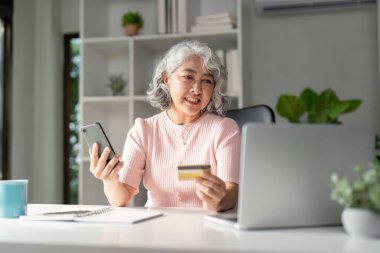 Yaşlı bir kadın rahat çalışma alanındaki kredi kartını güvenle kullanmaktan hoşlanıyor..